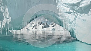 Close up iceberg arch at turquoise ocean bay with mountains on snow aerial. Environment preserve