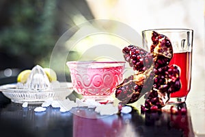 Close up of Iced tea of pomegranate and lemon on wooden surface in a transparent cup with entire ingredients with it i.e. sugar,po