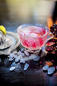 Close up of Iced tea of pomegranate and lemon on wooden surface in a transparent cup with entire ingredients with it i.e. sugar,po