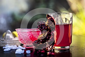 Close up of Iced tea of pomegranate and lemon on wooden surface in a transparent cup with entire ingredients with it i.e. sugar,po