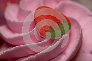 A close up of the icing and decoration of a strawberry cupcake using selective focus