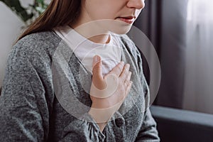 Close up of ill sad young caucasian woman putting hand on chest, feels discomfort. Having pain in chest, Gastroesophageal Reflux
