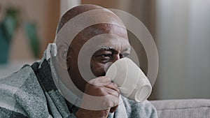 Close up ill sick elderly african american man covered with warm blanket sitting on couch in living room senior retiree