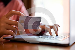 Close-up image. Asian woman holding her credit card and typing on laptop keyboard