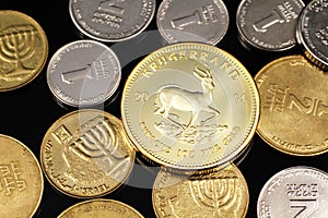 A close up image of an assortment of Israeli coins with a gold South African krugerrand on a black background