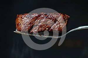 Close-up image of beef medium rare steak slice on a fork on dark background