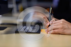 Close up image of businessman writing on an adhesive note at table in office