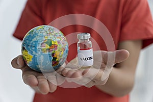 Close up image of child`s hands holding toy globe in one hand and ampoule with vaccine on another.