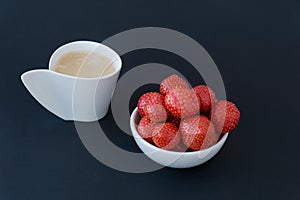 close up image of cup of coffee in white coffee cp and little round plate with bright juicy tasty strawberries.