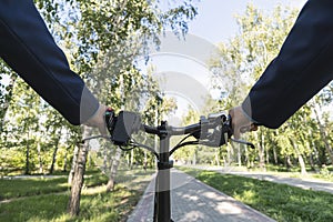 Close-up image of cyclist man hands on handlebar riding electric bike in park, face is not visible.Young man riding bike