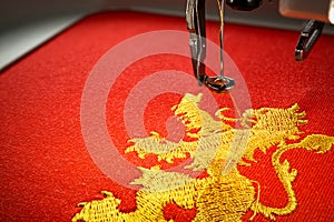 Close up image of embroidery machine and embroider gold lion on red fabric