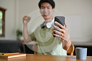 Close-up image of an excited young Asian man raises his hand, celebrating a sports match win