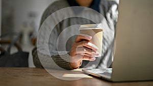 Close-up image of a female freelancer sipping coffee while responding to emails on her laptop