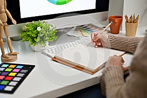 Close-up image of a female graphic designer or editor taking her creative ideas on her notebook