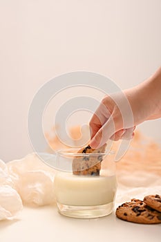 Female hand holding cookie and dipping in a warm milk