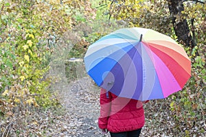 Close up image of female hiden under big colorful umbrella in autumn park