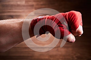 Close up image of fist of a boxer with red bandage against brown background.