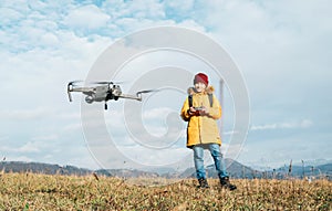 Close up image of flying drone with Teenager boy dressed yellow jacket on background piloting a modern digital drone using remote