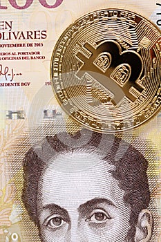 A golden bitcoin against a 100 Venezuelan Bolivares bank note photo
