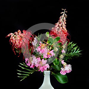 Close up image of Grevillea and Lantana flowers in a white vase isolated on black background