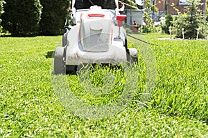 Close up image of grey electric lawn mower cutting green grass in garden.