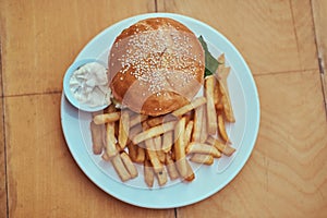 Close-up image of a hamburger with French fries and spicy sauce on a white plate. Unhealthy food concept