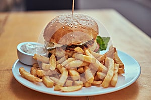 Close-up image of a hamburger with French fries and spicy sauce on a white plate. Unhealthy food concept