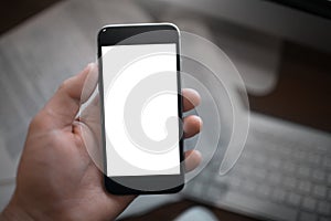 Close-up image of hand holding smartphone with blank mockup on paper background