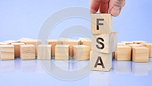 close up image hand of a young businessman holding a wooden cube with letter F. FSA on wooden cube on a blue background