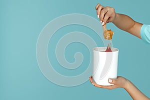 Close-up image of hans holding bucket with sugaring paste for depilation procedure over blue background.