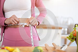 Close-up image of a healthy and slim woman in sportswear measuring her waist with a measuring tape