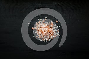 Close-up image of Himalayan salt grains on black wood background, view above