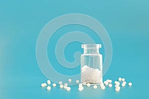 Close-up image of homeopathic globules in glass bottle on blue background. Homeopathy pharmacy, herbal, natural medicine