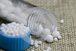 Close up image of Homeopathic granules in small bottle cap and medicine bottles with some pills scattered on jute sack background