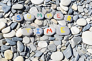 close up image of inscription summer time made with colorful letters written on stones, which lie on gray stones background.