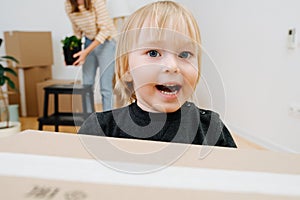 Close up image of jolly blond little son helping his mother with carrying boxes