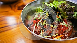 Close up image of Korean traditional food, spicy cold soba noodles, Bibim Guksu, on a stainless steel bowl