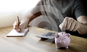 Close-up image of man hand putting coins in pink piggy bank for account save money.
