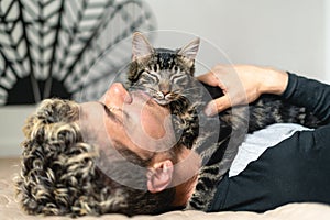 Close up image of man sleeping with his tabby cat on bed. Cat is posing above human. Love and care for animals concept