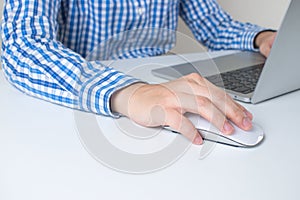Close-up image of a man wearing a blue plaid shirt using a hand holding the mouse in the office