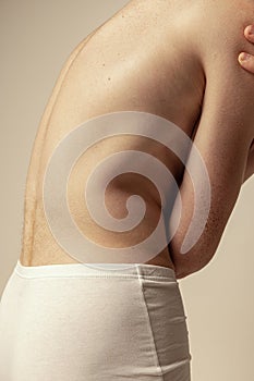 Close-up image of muscular male back isolated over grey studio background. Model posing in underwear. Freckled body