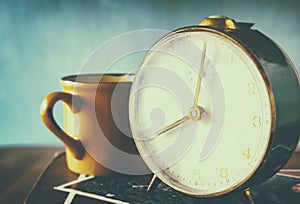Close up image of old clock and cofee cup over wooden table. image is filtered with retro faded style