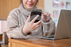 Close-up image of a positive Asian woman is checking messages on her phone while working indoors