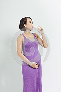 Close-up Image of pregnant woman Holding a glass of fresh milk and touching her belly with hands on white background