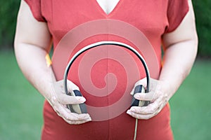 Close-up image of pregnant woman in red maternity clothes holding headphone on her baby bump.