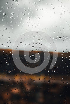 Close up image of raindrops on the window with cloudy sky on background. Vertical image of rain drops on the glass with outdoor on