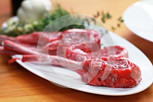 Close up image of Raw beef bone rib-eye steak on a plate with onion, garlic and garnish ready to cook on a wooden table