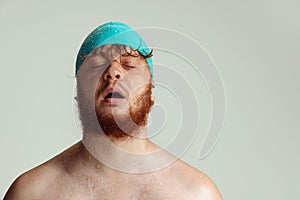 Close-up image of red-headed man in swimming hat posing isolated on gray studio background. Concept of sport, humor and