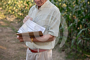 A senior Asian farmer or corn farm owner reading some papers, working in a corn field