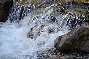 Close-up image of a small wild waterfall in the form of short streams of water between mountain stones